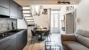 A modern kitchen with dark cabinets, a dining area with a round table and chairs, a sofa, and a staircase leading to another room. - Maison Beata - Two Bedroom Apartment, Sleeps 5 (Avola)