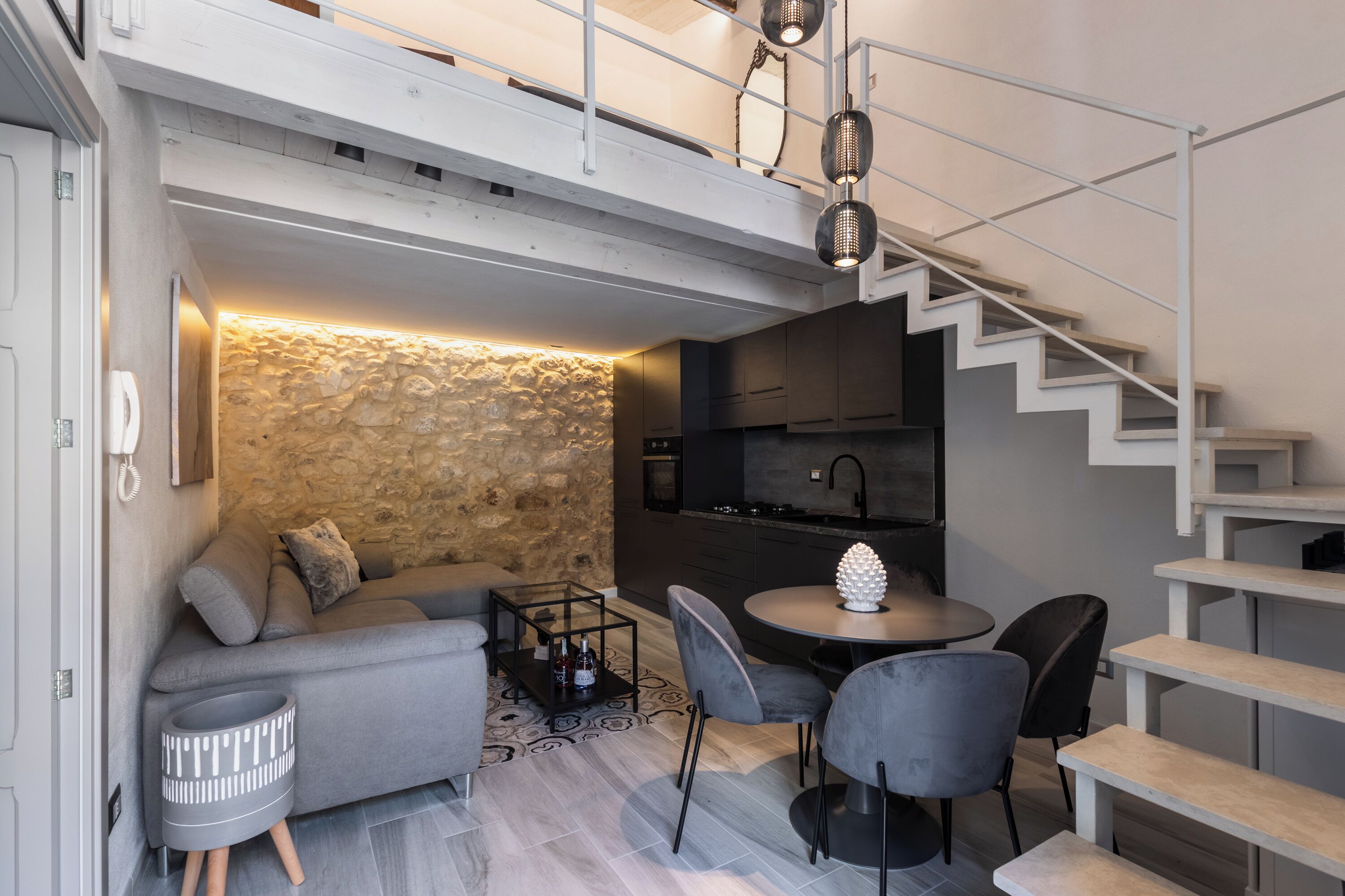Espaço compacto com parede de pedra decorativa, um sofá, uma mesa de jantar e uma escada.