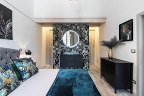 Une chambre à coucher moderne avec un lit, une commode, une coiffeuse avec un miroir et un mur recouvert d’un papier peint aux motifs tropicaux.