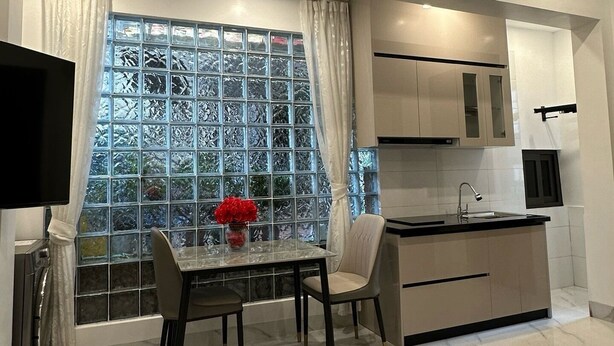 A modern kitchen with a marble countertop, a dining area with a glass table, and a large window with patterned glass. - Homestay-Kim Mã -Giang Văn Minh (Hanoi)