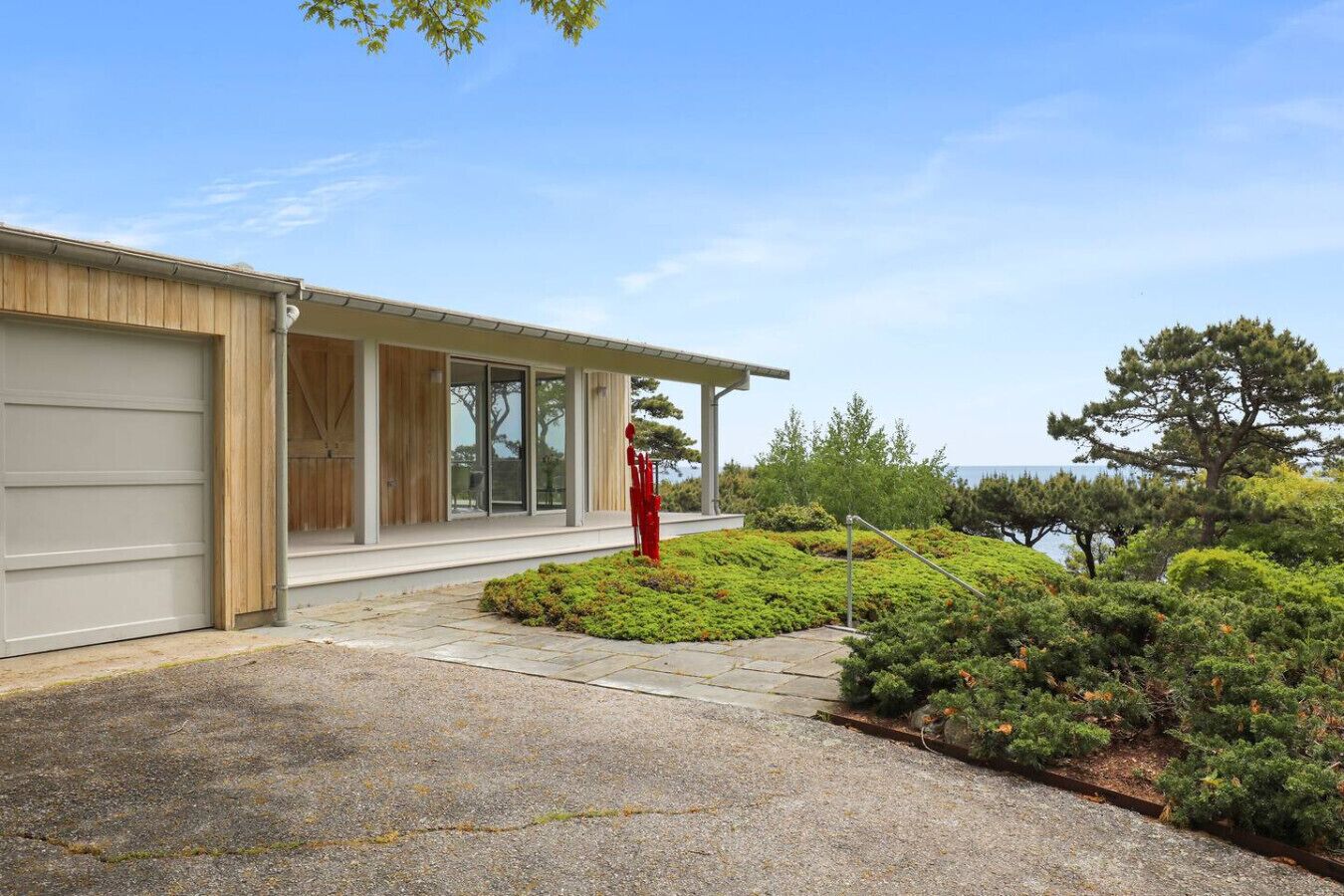 Une maison moderne dotée d’un garage, d’un porche abrité et d’un jardin aménagé offrant une vue sur l’océan.
