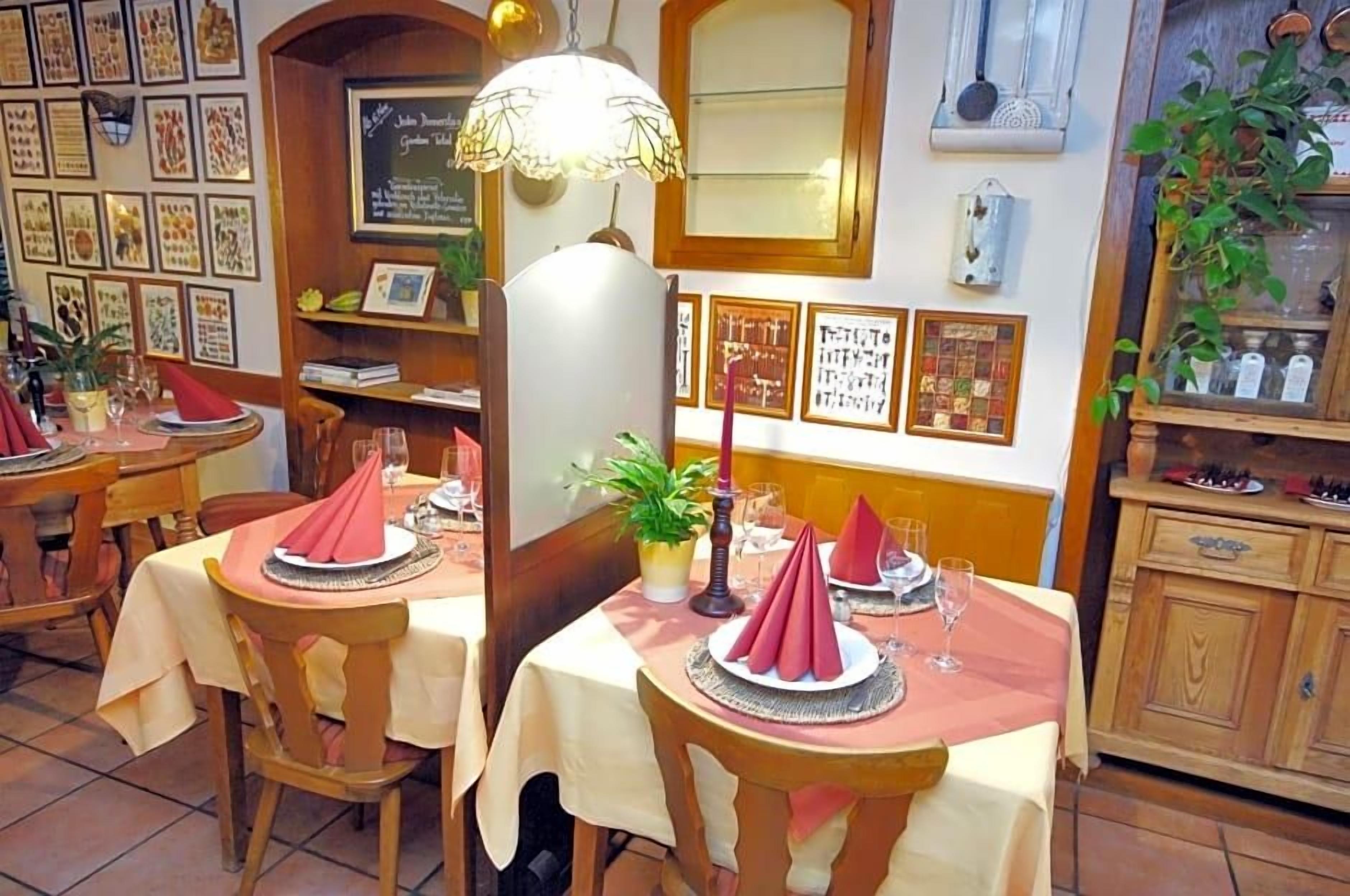 A restaurant interior with multiple tables, each set with red napkins, glasses, and a central plant.