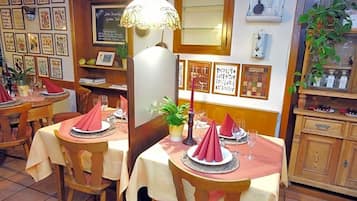 A restaurant interior with multiple tables, each set with red napkins, glasses, and a central plant.