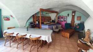 Ein Essbereich mit langem Tisch und Stühlen, eine Küche mit Bar und ein Wohnbereich mit Sofa und Uhr.