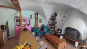 Ein gemütliches Wohnzimmer mit einer hölzernen Bank, einem blauen Sessel, einem pinken Schrank und einem Holzregal mit Büchern und Dekoration.