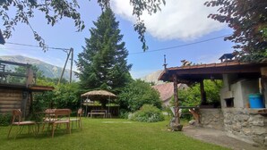 Ein rustikaler Außenbereich mit Holztisch und -stühlen, einem Strohdachschirm und einer Steinmauer.