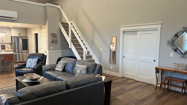 A living room with a gray leather sofa, a black leather chair, and a wooden coffee table. A staircase leads to an upper level.