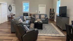 A spacious living room with a sectional sofa, two recliner chairs, a coffee table, and a television on a cabinet.