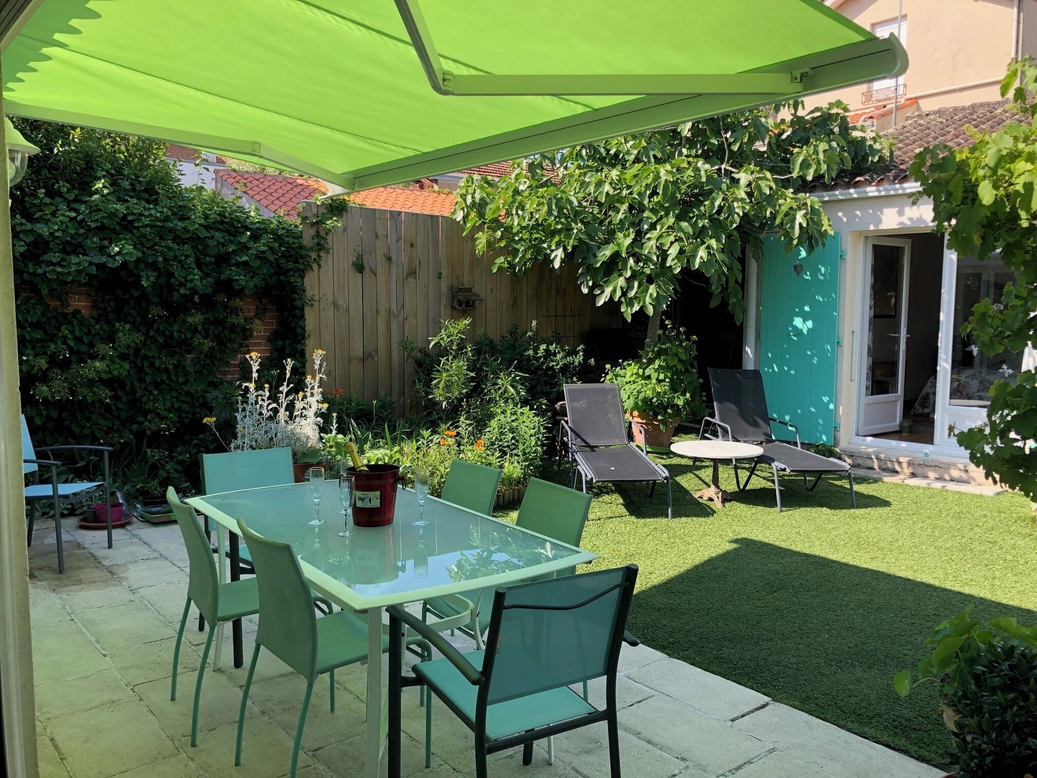 A patio with a glass table and chairs, a wooden fence, and a green umbrella.