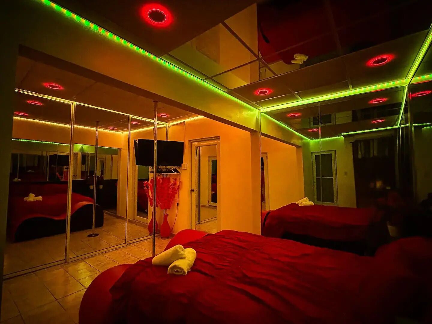 A room with mirrored walls, red bedding, and LED strip lighting.