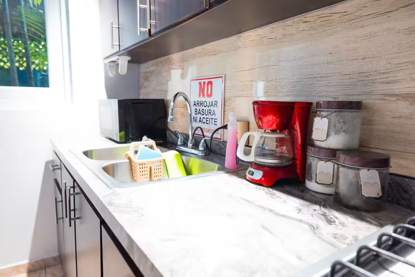 Una cocina con un lavamanos, una cafetera y un cartel que dice "NO ARROJAR BASURA NI ACEITE".