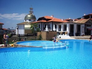 A swimming pool with a fountain, surrounded by buildings with red roofs and a white dome structure. - Breeze Apartments (Sveti Vlas)