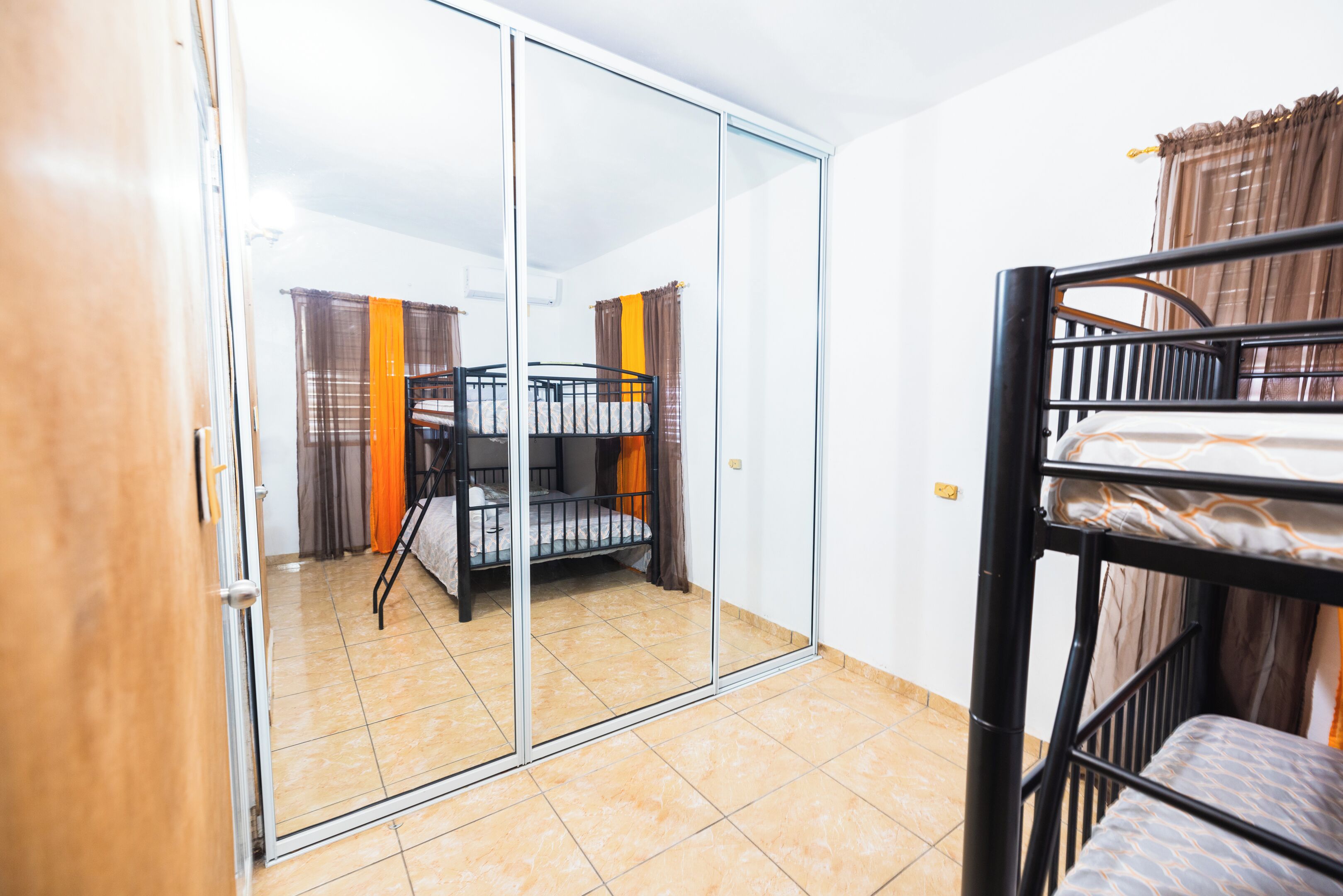 Une chambre avec un lit superposé, une porte-fenêtre coulissante et un sol carrelé.
