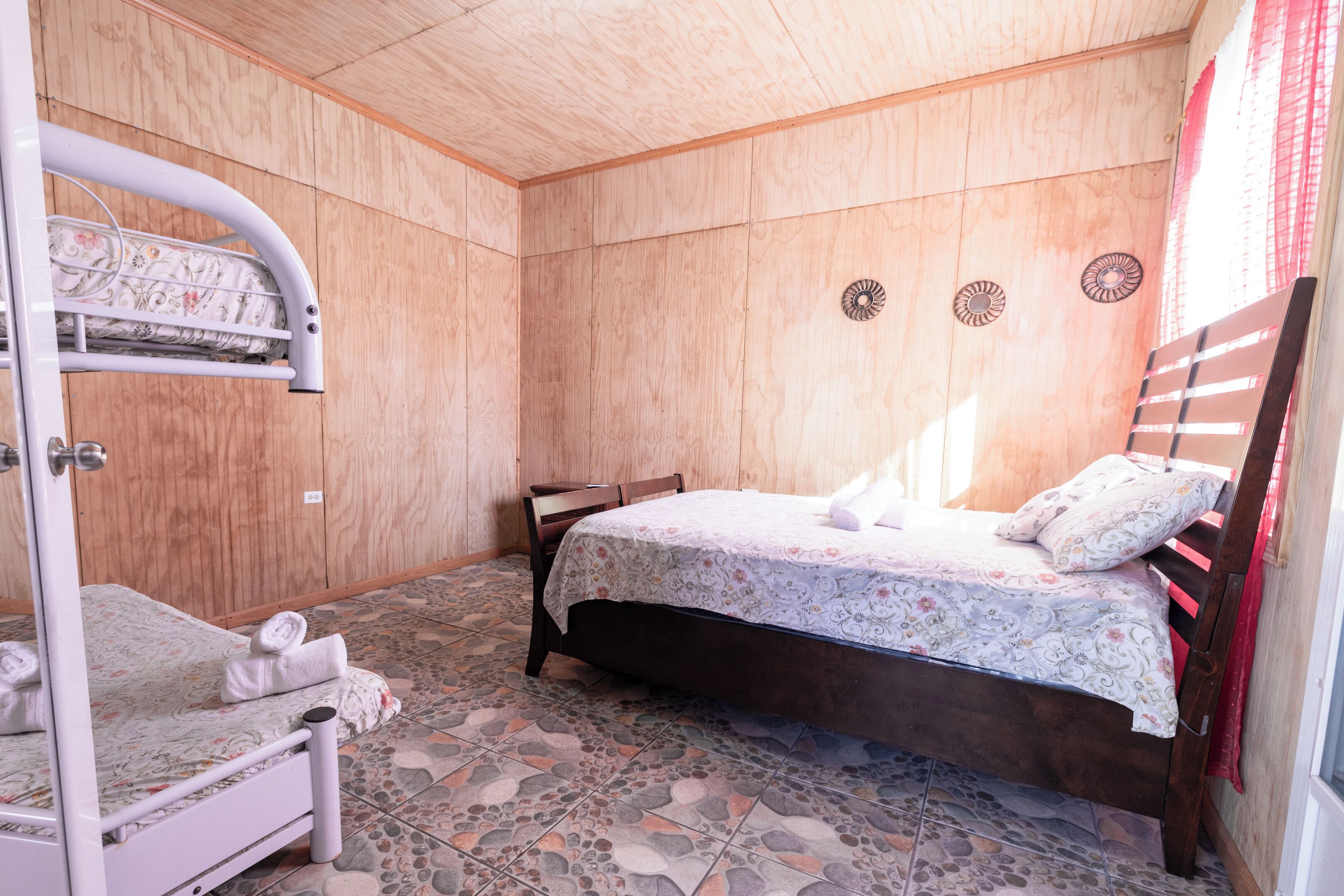 A room with a bunk bed, a single bed, and a wooden wall.