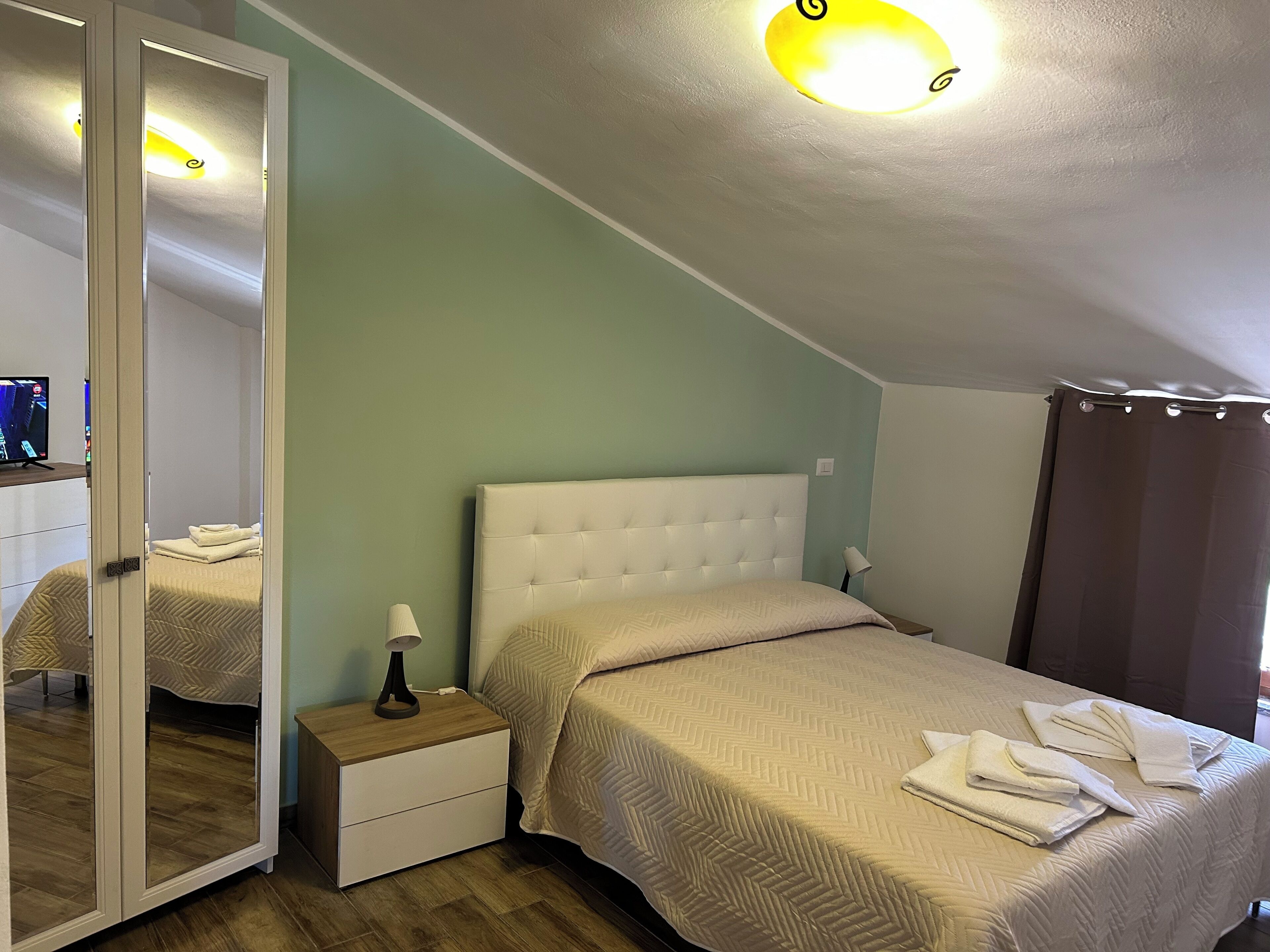 Una camera da letto con un letto, un comodino, uno specchio e una lampada a soffitto.