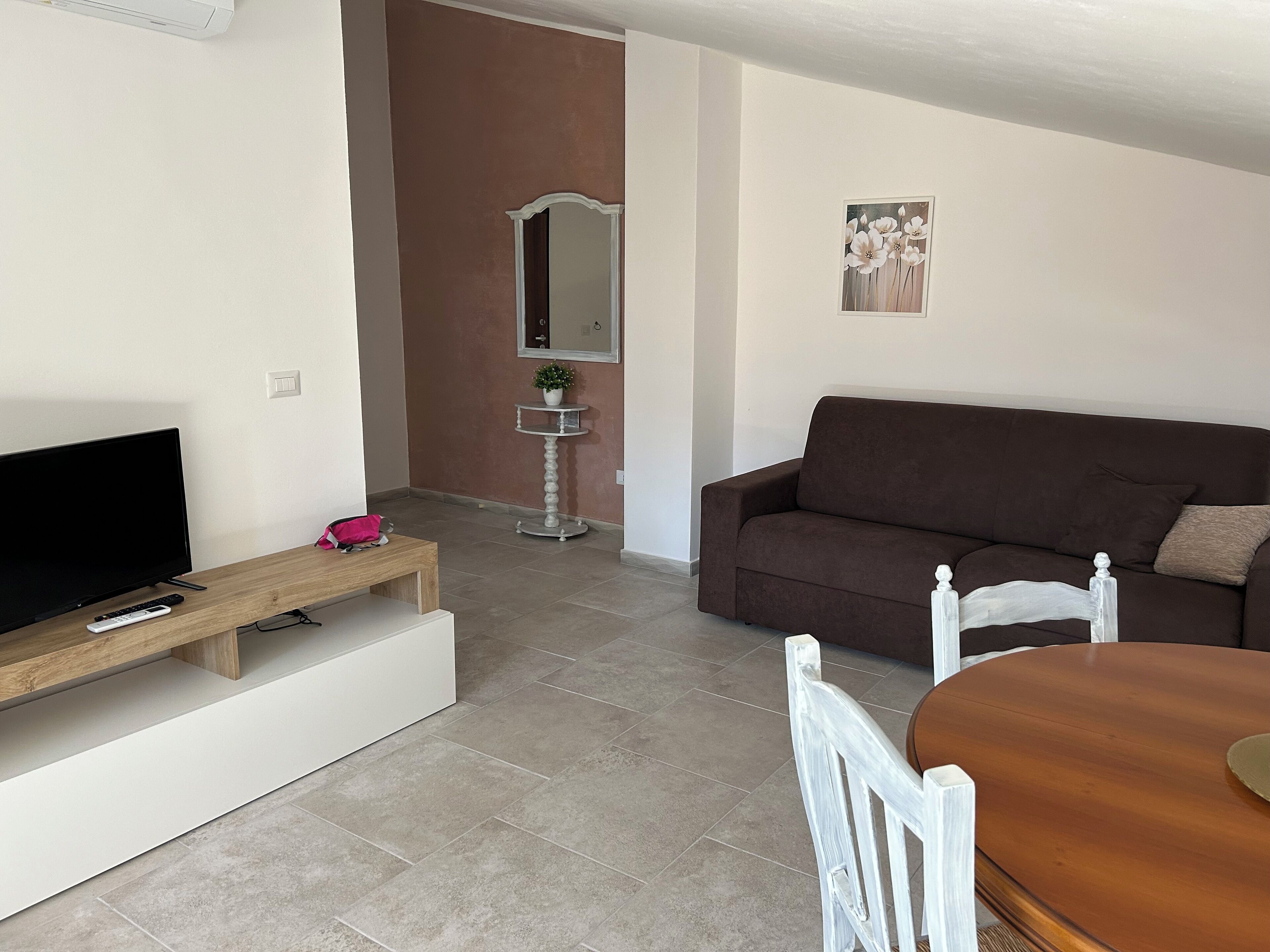 Un salon avec un canapé marron, une table basse en bois, un téléviseur et une table à manger avec des chaises.