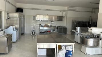 A commercial kitchen with stainless steel appliances, a central island, and a flat-screen TV mounted on the wall.