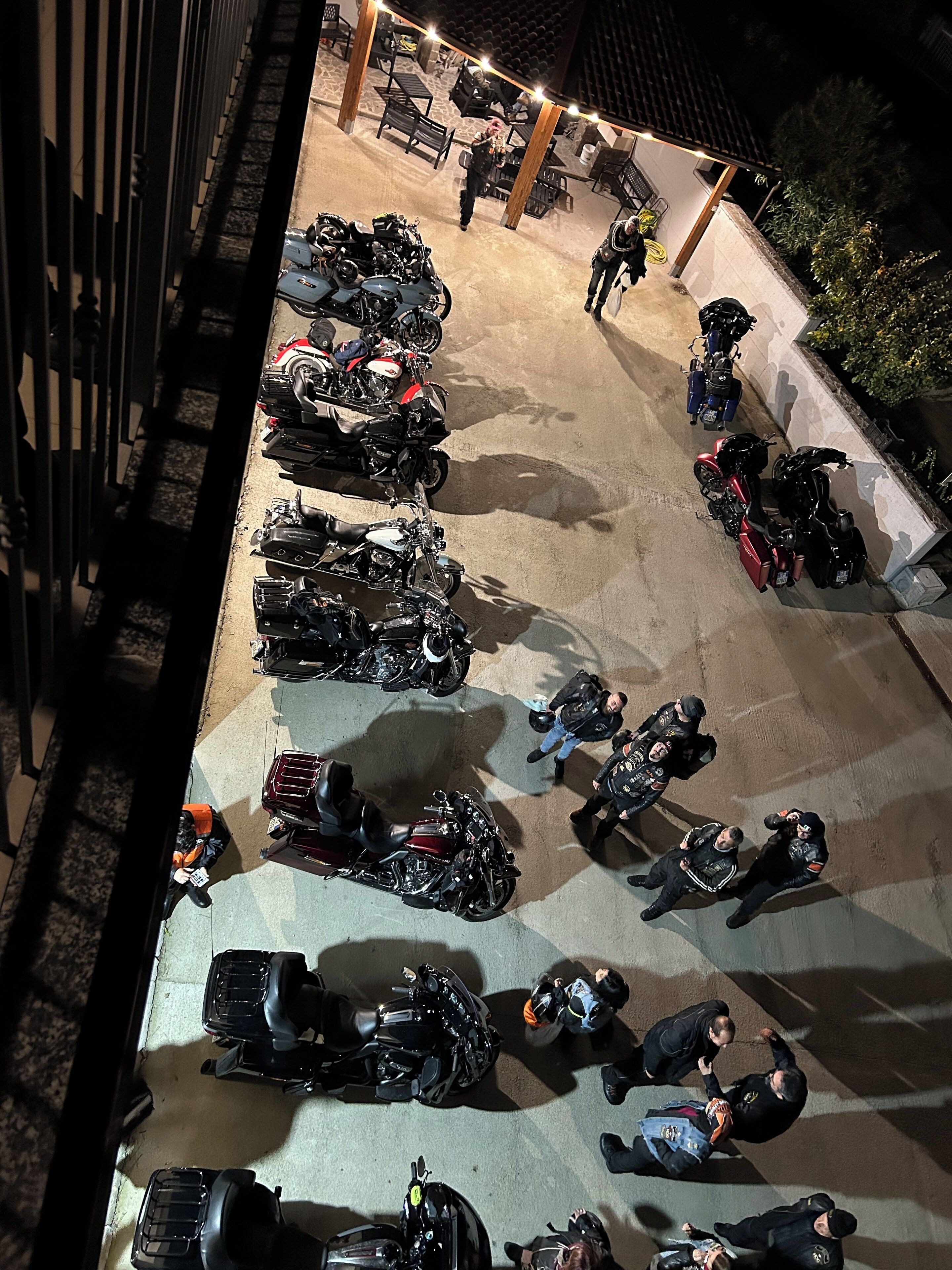 A parking area with multiple motorcycles and a few people.