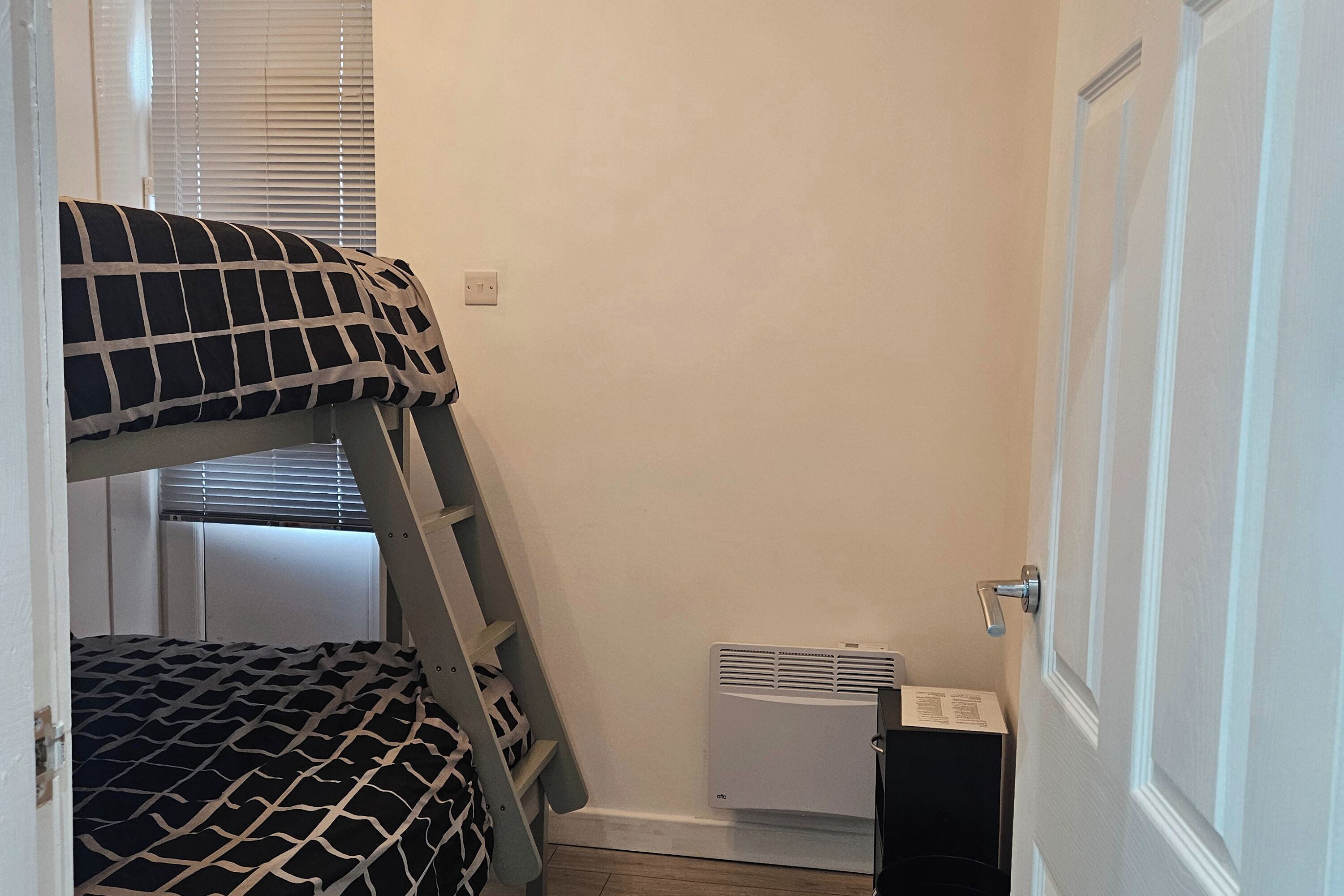Ein Zimmer mit Etagenbetten, einer Stehleiter, einem Heizkörper und einer Tür.