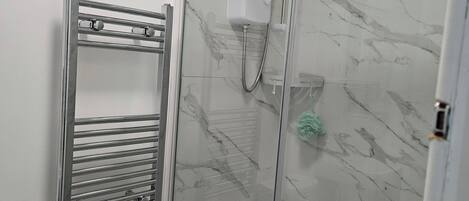 A bathroom with a glass-enclosed shower, a chrome towel rack, and a white shower control panel.
