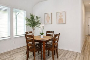 A dining area with a wooden table and chairs, a potted plant, and two framed artworks on the wall. - Modern 3 BR New House with Grill and Games (Pattison)