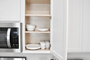 A kitchen with a microwave, shelves with plates and cups, and a cabinet door.