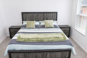 A bedroom with a bed, two nightstands, a window with blinds, and a carpeted floor. - Modern 3 BR New House with Grill and Games (Pattison)