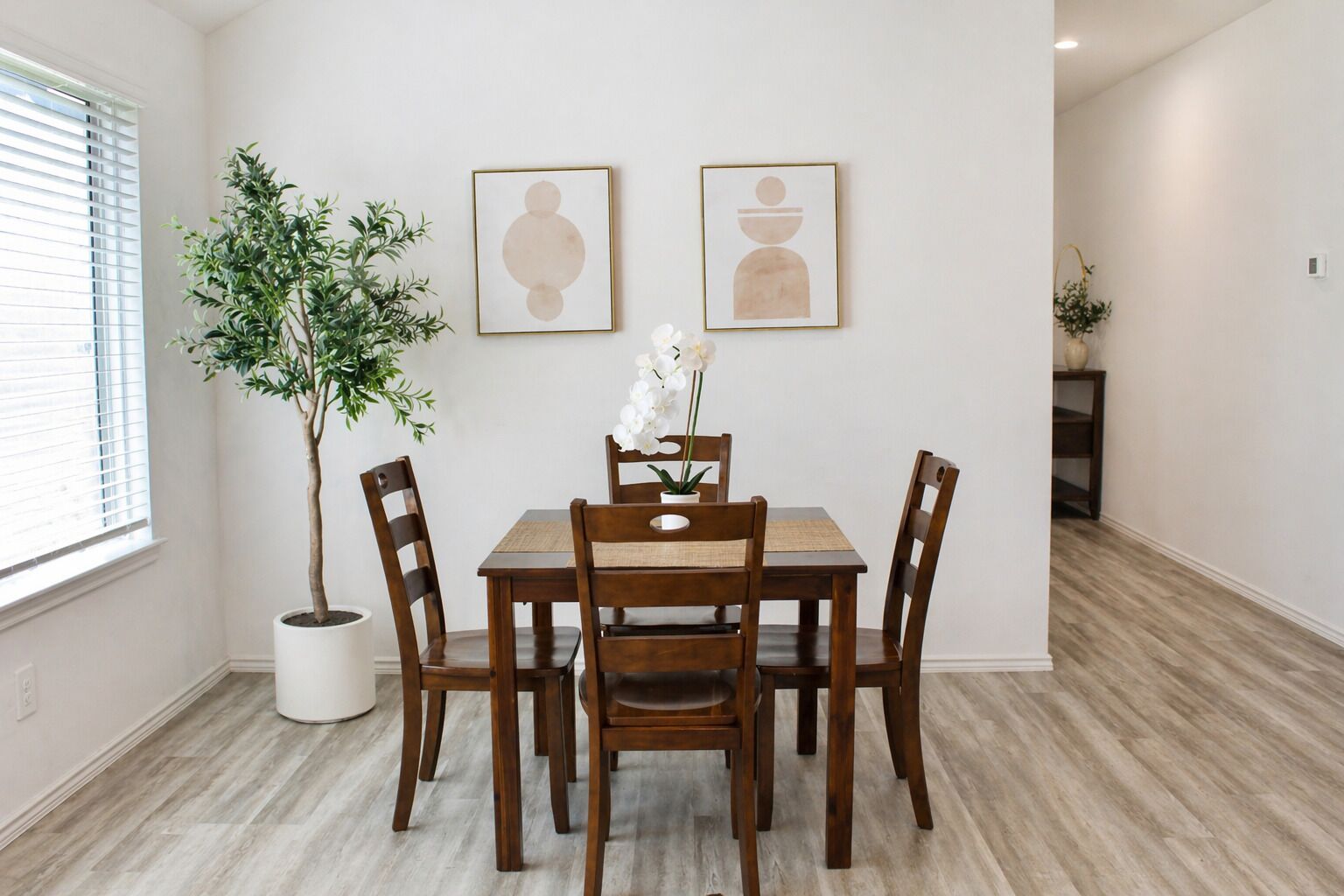 Un coin repas avec une table et des chaises en bois, une plante en pot et deux œuvres d’art encadrées accrochées au mur.