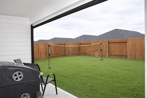 Un jardin avec une pelouse artificielle, un barbecue, une barrière en corde et une clôture en bois.