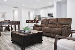 A modern living room with a brown sofa, a wooden coffee table, and a dining area with a wooden table and chairs.