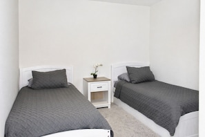Une chambre double avec deux lits simples, une petite table de chevet avec un tiroir et une plante en pot.