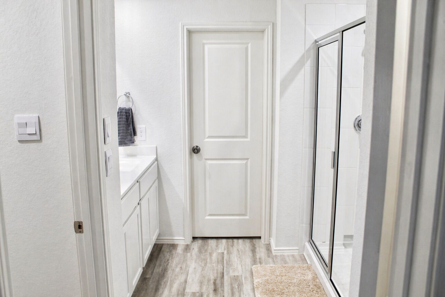 A hallway with a white door, a small sink, and a shower area.