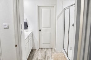 A hallway with a white door, a small sink, and a shower area.