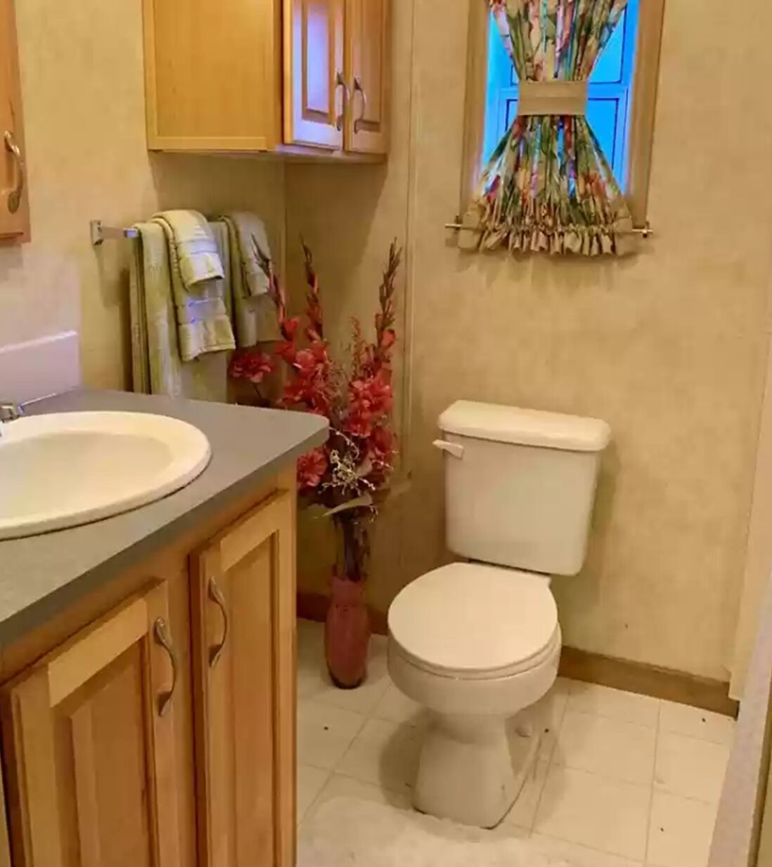 A bathroom with a sink, toilet, wooden cabinets, and a window with curtains.