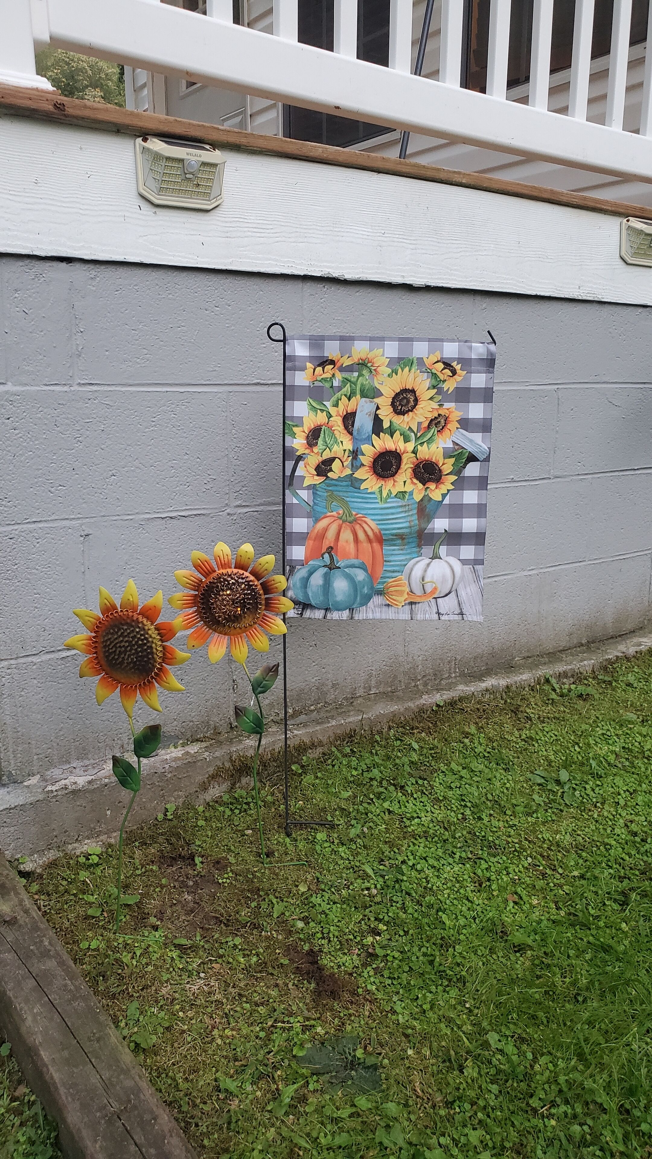 Een muur met een muurschildering van zonnebloemen en pompoenen, een houten omheining en een metalen poort.