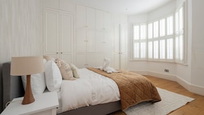 Un dormitorio con cama, mesita de noche, lámpara, ventana con persianas y armarios empotrados.