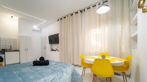 Quarto moderno com cama, escrivaninha e área de refeições.