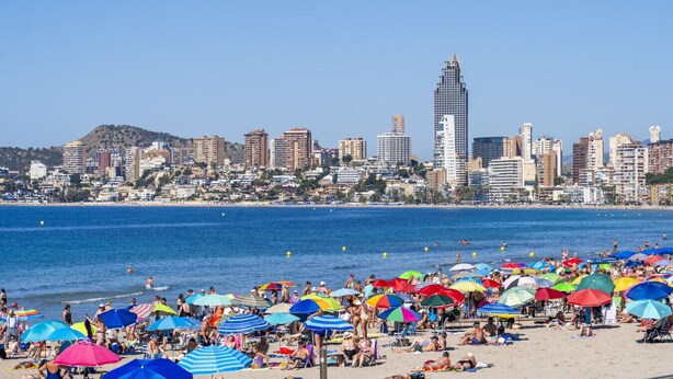 Uma praia com vários guarda-sóis coloridos e pessoas aproveitando o tempo ensolarado.
