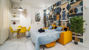 Quarto moderno com cama, cadeiras amarelas, uma mesa de jantar e uma grande pintura abstrata na parede.