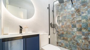 A modern bathroom with a white toilet, a blue cabinet, a white sink, a black faucet, a handheld showerhead, and a mosaic tile shower wall. - Brisas del Poniente-Deluxe Room Ocean View (Benidorm)
