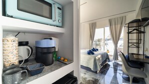 A compact kitchenette with a microwave, coffee maker, and storage containers. The room features a bed with a view of the outdoors. - Brisas del Poniente-Deluxe Room Ocean View (Benidorm)