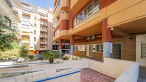 Un edificio residencial de varios pisos con balcones, un patio con plantas y un elemento acuático azul.