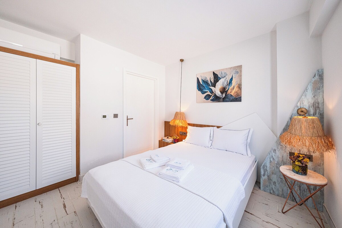 Un dormitorio ordenado con cama, lámparas de noche y un cuadro en la pared.