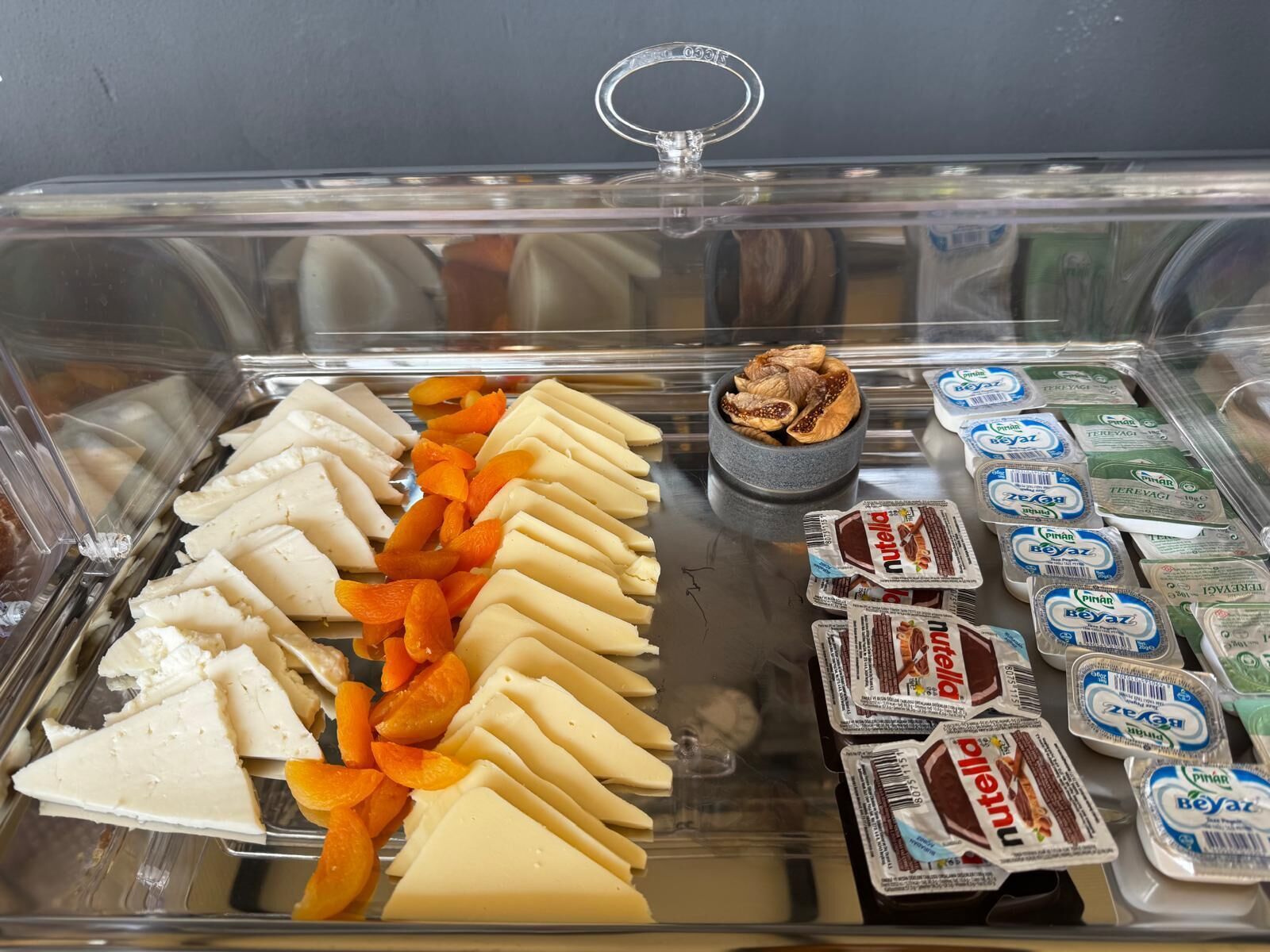 Una vitrina de exhibición de alimentos con varios quesos, frutas en rodajas y refrigerios envasados.
