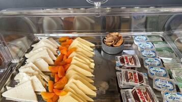 Una vitrina de exhibición de alimentos con varios quesos, frutas en rodajas y refrigerios envasados.