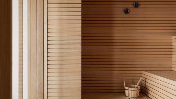 Una sauna con listones de madera, un banco y un cubo.