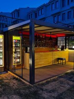 Uma área moderna de bar ao ar livre, com balcão de madeira, vitrines de vidro e um espaço para sentar.