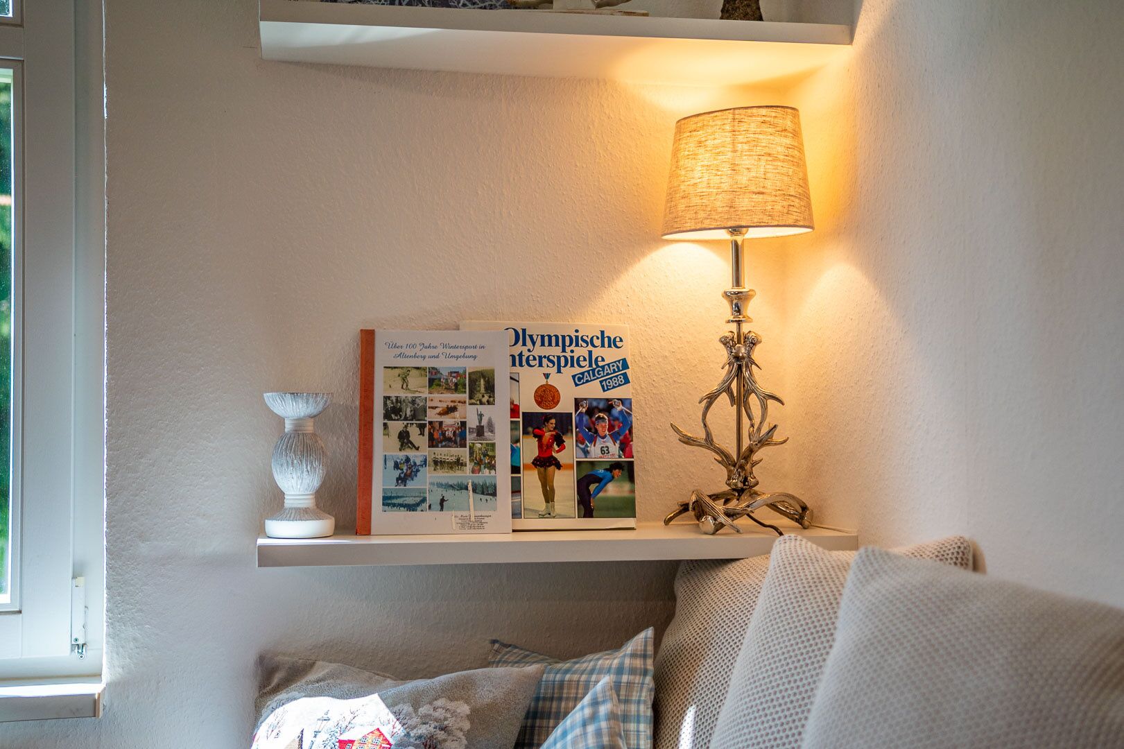 A shelf with a book titled 'Olympische Interziele Calgary 1988', a decorative lamp, and a white vase.