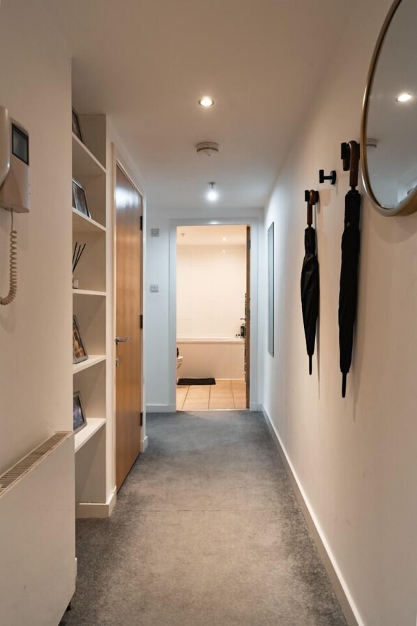 A hallway with a carpeted floor, a white wall with a mirror, and a door leading to a bathroom.