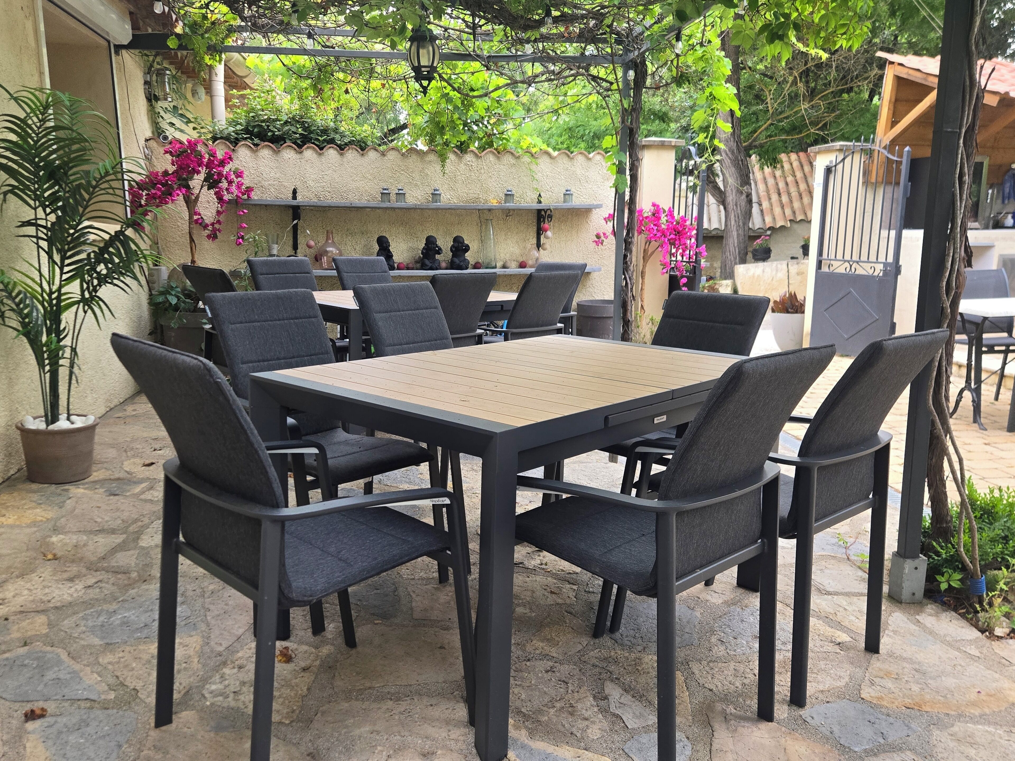 An outdoor patio with a table and chairs, surrounded by potted plants and a stone wall.